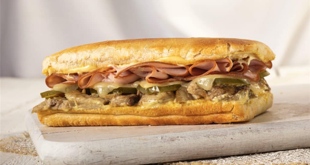 Experience the magic of Disney Springs with the Earl of Sandwich's New Sandwich—a warmly toasted creation stacked with ham, pickles, melted cheese, and savory beef, all served on a rustic wooden board.