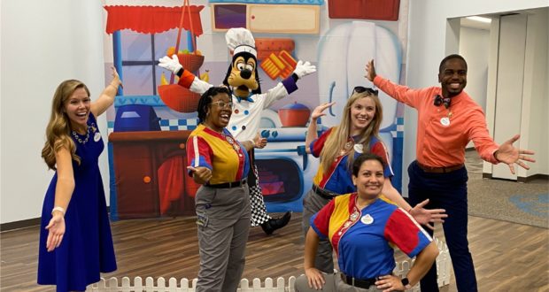 Goofy joins five enthusiastic fans for a cheerful group photo in front of a kitchen-themed backdrop at Disney, capturing a magical moment with one of the beloved characters.