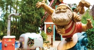 Santa rides the waves on a surfboard surrounded by dazzling Christmas decorations, with a colorfully decorated holiday house and camper in the background—capturing Disney’s signature blend of festive imagination and Florida fun during the holidays.