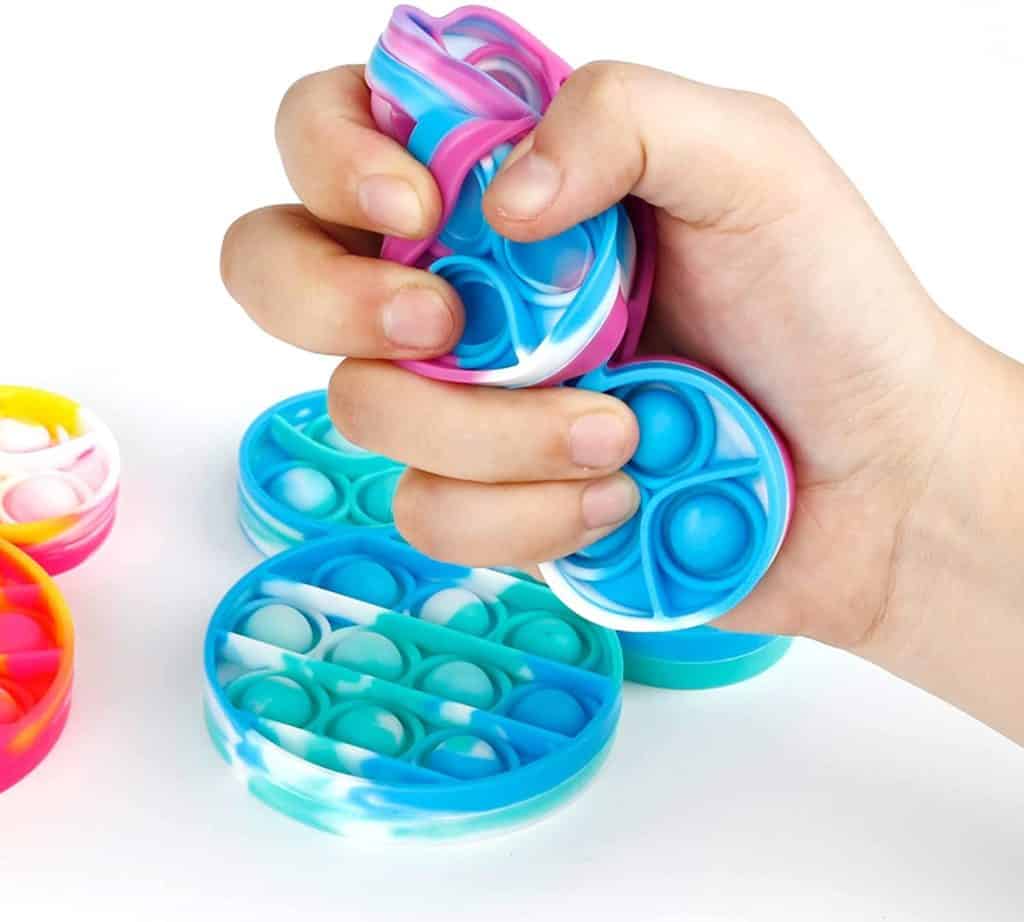 A guest’s hand squeezes a blue and pink tie-dye Mickey Mouse-shaped silicone bubble pop fidget at Disney World, surrounded by even more colorful pop fidgets—perfect for a magical day of fun and sensory play in the park.