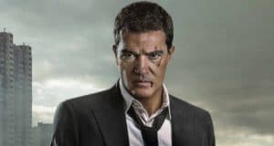 A sharply dressed man with his tie loosened channels the adventurous spirit of Antonio Banderas from Indiana Jones 5, posing seriously against a backdrop of towering city buildings and dramatic cloudy skies, evoking the excitement and cinematic atmosphere found at an epic movie-themed attraction.