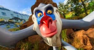 A vibrant baboon statue stands out in the midst of Walt Disney World Resort’s lively atmosphere, with colorful details and a backdrop of whimsical buildings and lush trees enhancing the park’s signature décor.