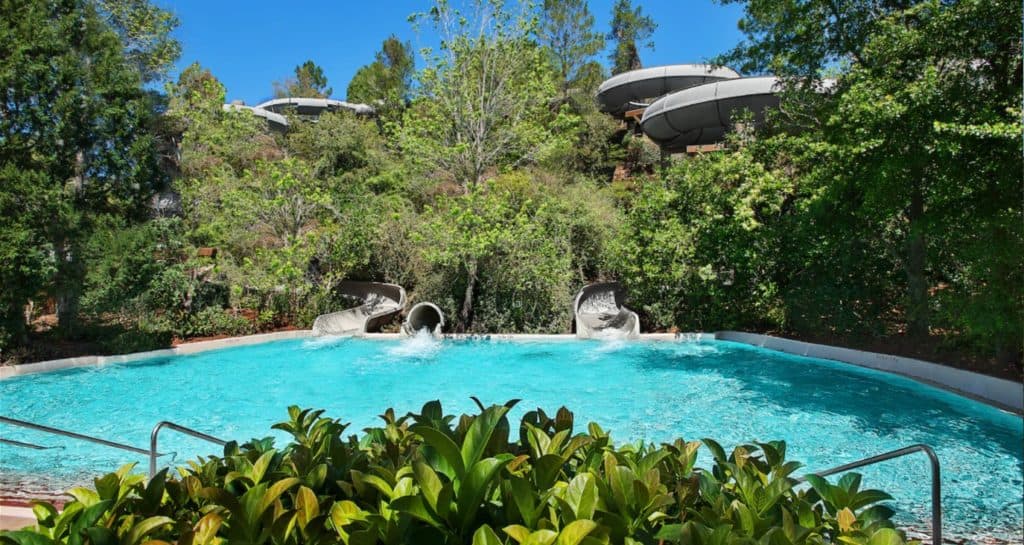 Three thrilling water slides plunge into a sparkling pool, surrounded by lush greenery and trees beneath a bright sky—a can’t-miss attraction at Disney’s Blizzard Beach Water Park.