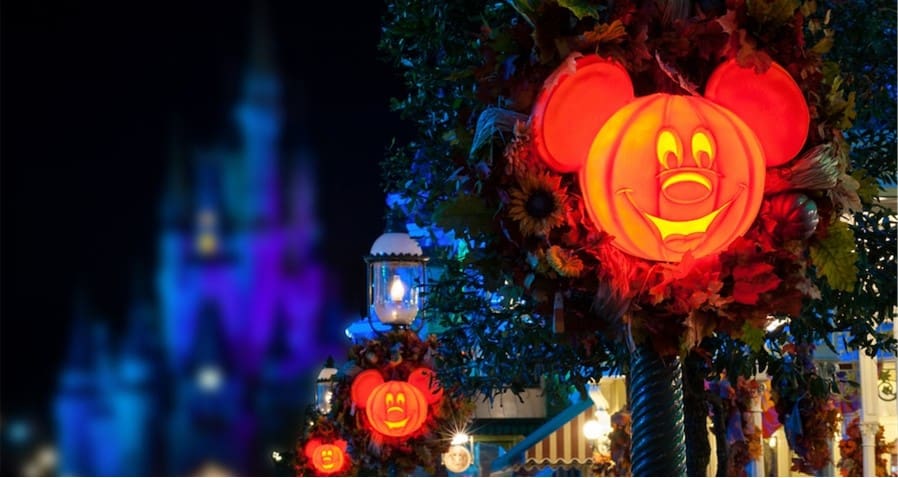 Festive Mickey Mouse pumpkin decorations illuminate the October night at Magic Kingdom, with Cinderella Castle glowing in blue and purple hues during Disney After Hours Boo Bash.