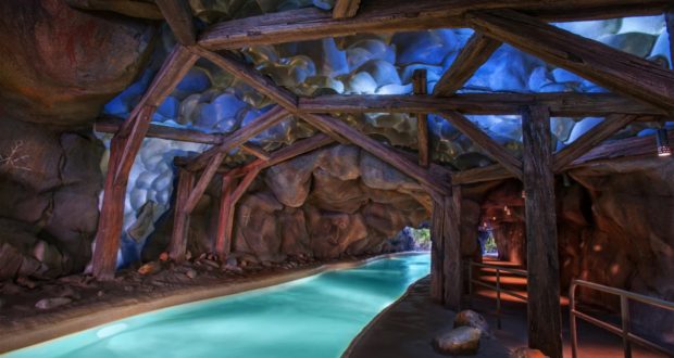 An enchanting blue river glides beneath rustic wooden beams inside a rocky cavern, capturing the magical vibe of a signature Disney Water Park attraction—just like drifting through Blizzard Beach’s must-see indoor adventure.