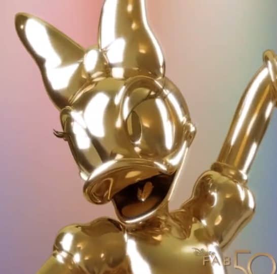 Daisy Duck’s golden Fab 50 statue at Walt Disney World, featuring her signature big bow as she smiles and waves against a vibrant gradient backdrop.