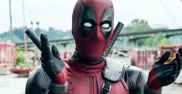 Deadpool, clad in his iconic red and black suit, strikes an animated pose with both hands as he entertains fans on a dynamic bridge set within a lively Marvel-themed attraction, channeling the limitless fun of the Deadpool multiverse.