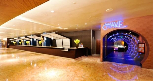 Modern hotel lobby featuring a lengthy check-in desk and the eye-catching neon "WAVE" sign marking the entrance to its trendy club, all showcasing upgrades from August 2021 just minutes away from Walt Disney World.