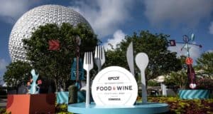 Oversized utensils create a playful frame around the Epcot Food & Wine Festival sign, with Spaceship Earth rising in the background—an iconic photo opportunity for Disney fans exploring Epcot during Extended Evening Hours.