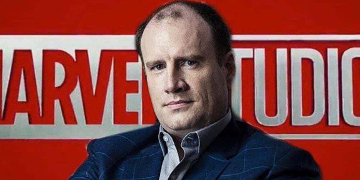 A man in a suit poses in front of a large red and white Marvel Studios logo background.