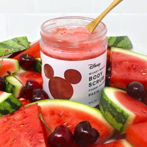 Cherry watermelon body scrub in a jar, surrounded by juicy watermelon slices and bright cherries, with a wooden spoon inside—fresh from our Disney Springs-inspired collection. Experience the magic of the parks at home and pair it with Mickey Mouse Soaps for a spa day worthy of your favorite Disney destination!.