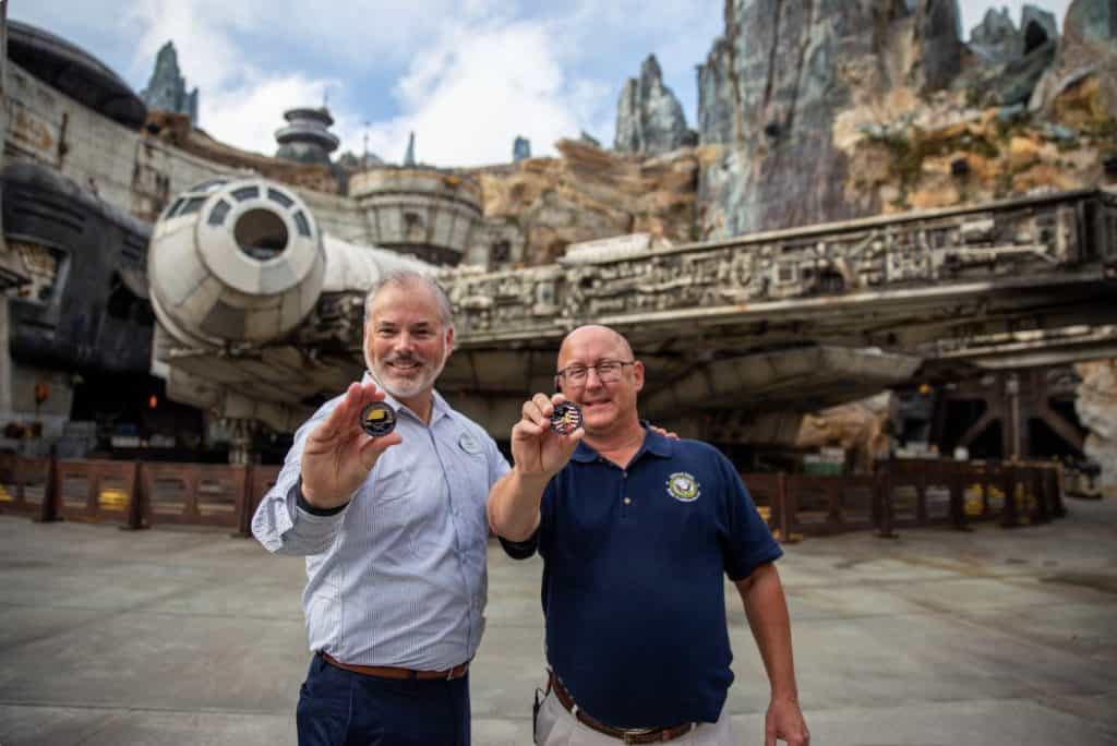 Guests beam with excitement as they display collectible coins in front of the impressive Spaceship Earth at EPCOT in Walt Disney World.