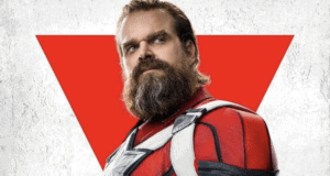 Red Guardian strikes a heroic pose in his signature red suit, standing proudly before a bold red triangle backdrop on a crisp white stage, ready for action-packed adventures at the Marvel-themed attraction.