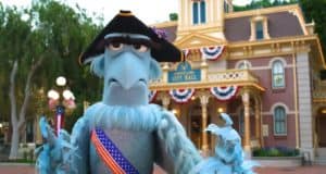 Sam Eagle, the blue muppet known for his patriotic flair, appears in colonial attire in front of Disneyland’s City Hall, which is festively decorated with Disney’s red, white, and blue banners in celebration of the Fourth of July.