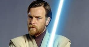 Obi-Wan Kenobi, as seen in his signature Jedi robes and wielding a blue lightsaber, strikes a serious pose against a plain backdrop, capturing the look of Rupert Friend's portrayal.