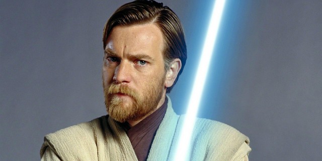 Obi-Wan Kenobi, as seen in his signature Jedi robes and wielding a blue lightsaber, strikes a serious pose against a plain backdrop, capturing the look of Rupert Friend's portrayal.