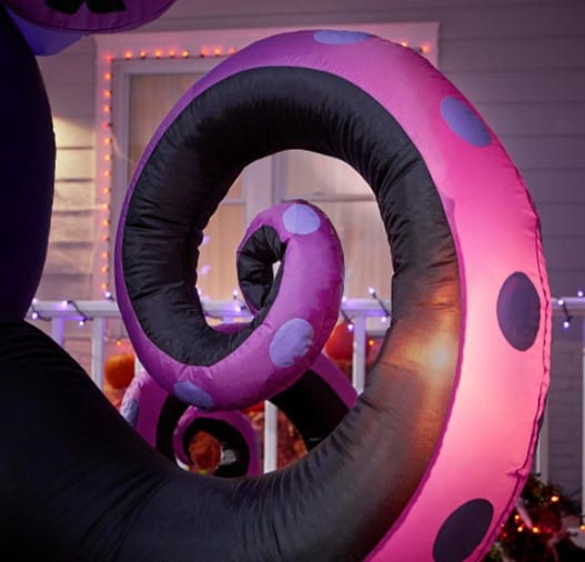 An eye-catching pink and black inflatable tentacle with vibrant purple spots—evoking the style of Ursula from Disney’s The Little Mermaid—looms dramatically in front of a festively lit house, creating a Halloween display worthy of any theme park attraction.