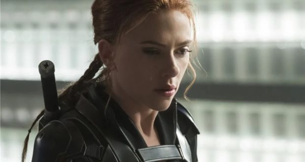 A Cast Member with braided red hair in a sharp black suit stands backstage at Disney, looking down thoughtfully and seriously, as if reflecting on recent industry buzz among Imagineers and Executives about the ScarJo lawsuit’s impact on future theme park entertainment deals.