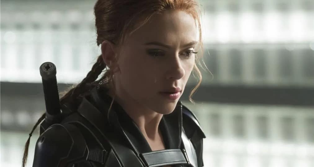 A Cast Member with braided red hair in a sharp black suit stands backstage at Disney, looking down thoughtfully and seriously, as if reflecting on recent industry buzz among Imagineers and Executives about the ScarJo lawsuit’s impact on future theme park entertainment deals.