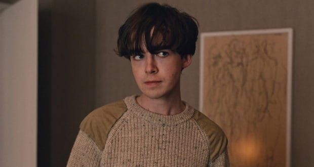 A guest with dark hair, channeling Alex Lawther’s look, dressed in a beige sweater and posing indoors against a gallery-style backdrop, capturing the cinematic ambiance reminiscent of Star Wars: Andor within an immersive themed entertainment space.