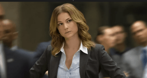 A confident woman with wavy hair wearing a suit jacket strikes a Sharon Carter–like pose, hands on hips and gazing to the side amidst the bustling crowd at Avengers Campus.