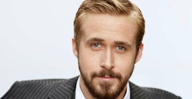 A sharp-dressed man with short blond hair, beard, and mustache channels the style of Ryan Gosling in a pinstripe suit, engaging guests with a direct gaze like he’s about to step onto the stage for an MCU fan event at a major theme park.
