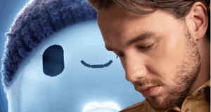 A guest stands thoughtfully beside a cheerful blue cartoon character wearing a beanie, capturing the playful spirit of Ron's Gone Wrong at an entertainment venue.
