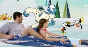 Guests aboard the Disney Wish experience the AquaMouse attraction, gliding past animated scenes featuring a playful yeti, winter-clad Disney mice, and a lively dog character, all set amid the whimsical magic that defines Disney Cruise Line entertainment.