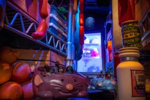 Remy’s Ratatouille Adventure in EPCOT’s France Pavilion invites Disney fans to hop into rat-shaped ride vehicles and scurry through an oversized kitchen, racing past enormous food props and larger-than-life bottles—just like the scenes captured in the latest attraction photos!.