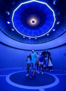 Guests gather beneath the iconic glowing blue orbital ceiling inside Space 220 Restaurant, immersing themselves in the futuristic dining experience at EPCOT.