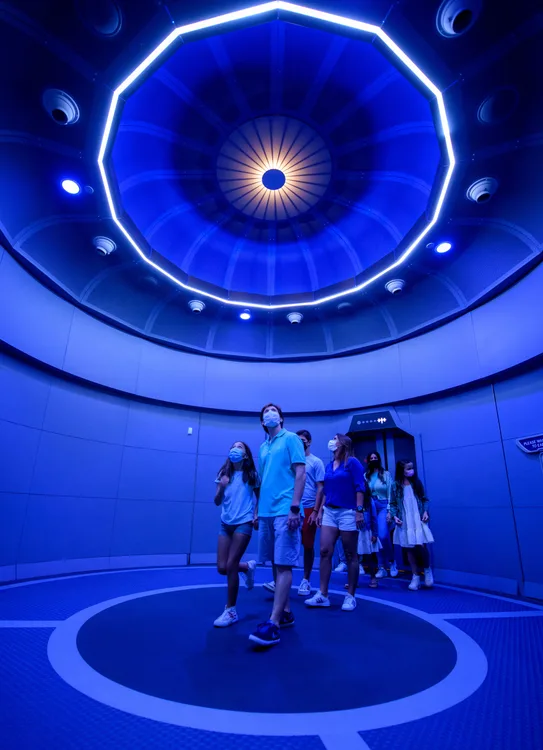 Guests gather beneath the iconic glowing blue orbital ceiling inside Space 220 Restaurant, immersing themselves in the futuristic dining experience at EPCOT.