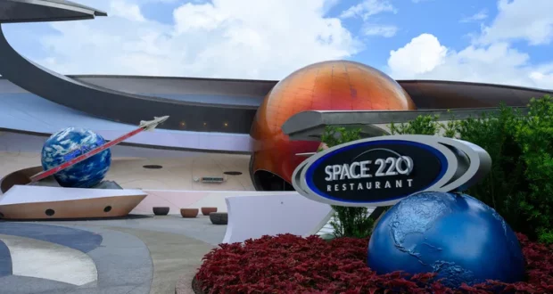 Entrance to Space 220 Restaurant at EPCOT, featuring impressive planet models and immersive space-themed decor against a bright blue sky, welcoming theme park guests to experience a galactic dining adventure.