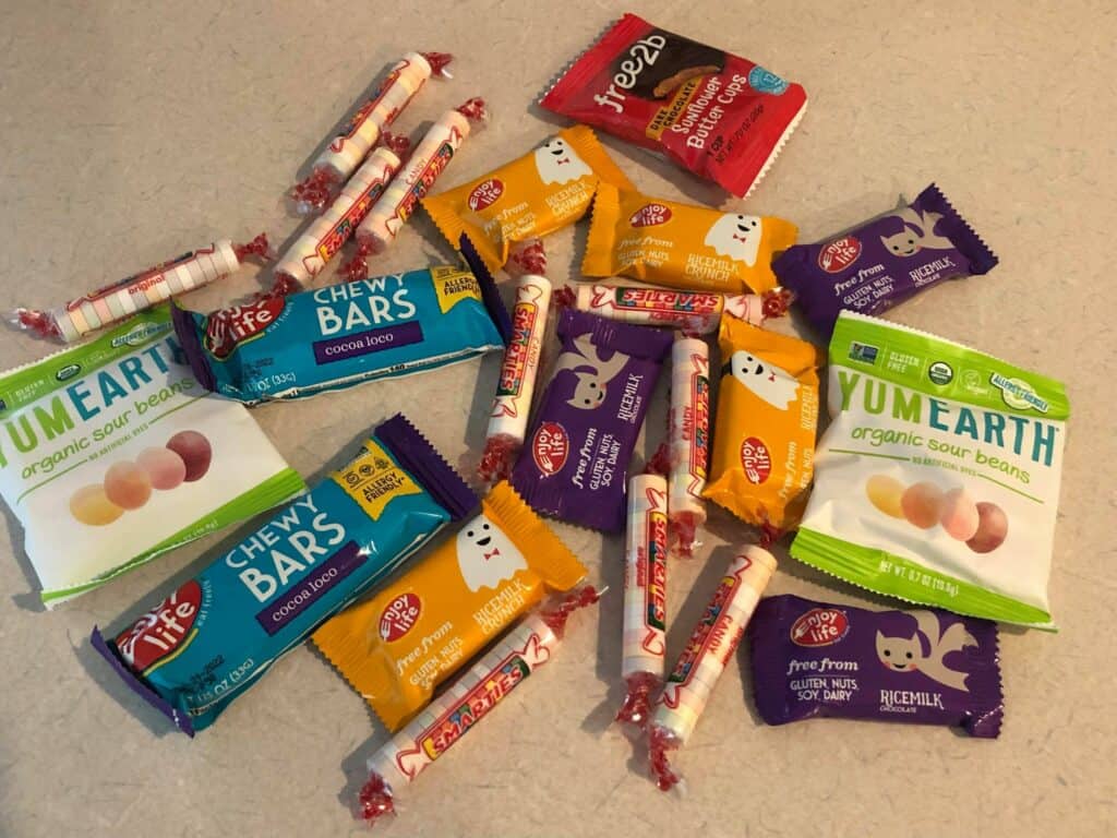 A festive assortment of allergy-friendly Halloween treats—like YumEarth candies, Enjoy Life bars, Smarties, and Free2b bites—specially selected for Disney After Hours Boo Bash guests. Features visible Allergy Information to keep your snacking magical and worry-free during the event.
