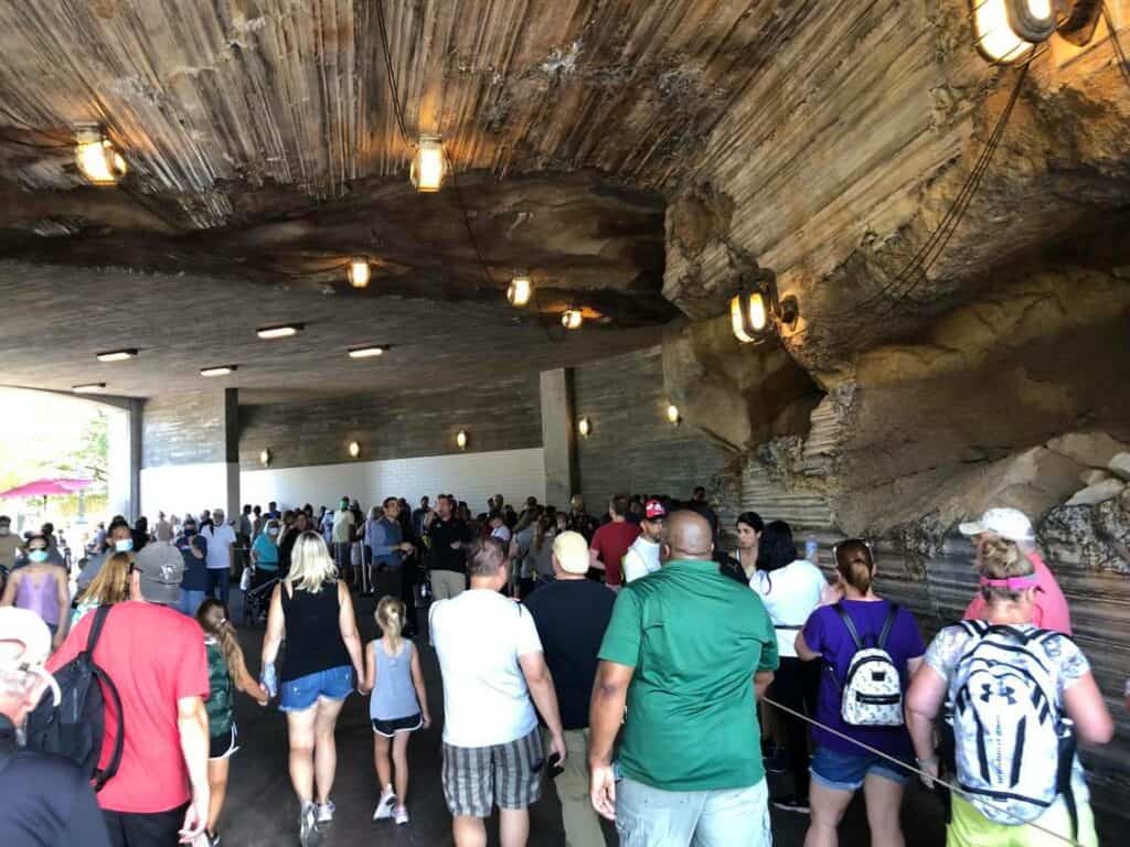 Guests make their way through the immersive, cavernous queue for Star Wars: Rise of the Resistance, strolling beneath hanging lights in a rocky tunnel. Ahead, crowds gather near the exit as fans eagerly await their turn on this iconic Disneyland attraction.
