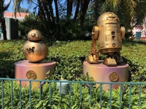 BB-8 and R2-D2, gleaming in gold as part of the Fab 50 Character Collection, welcome guests among lush greenery at Disney’s Hollywood Studios.