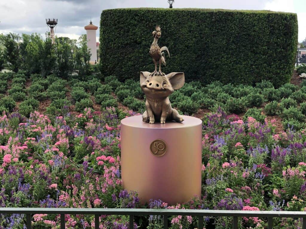 Pua and Hei Hei shimmer in bronze on their pedestal, nestled among vibrant pink and purple blooms at EPCOT. As part of the Fab 50 Character Collection, this delightful statue celebrates iconic Disney animation right in the heart of the park.