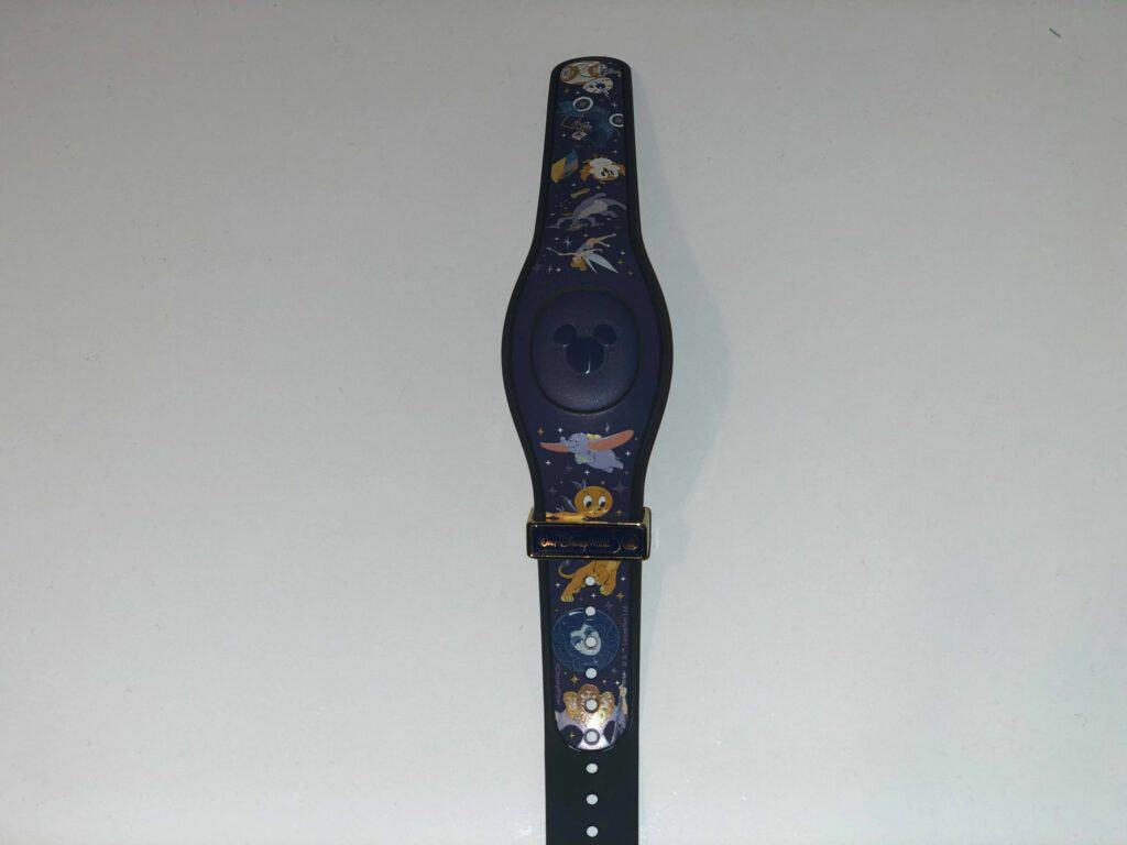 A Disney MagicBand featuring Pluto, Goofy, and stars rests on a white surface, ready to make your next visit extra magical. Watch your mailbox for this enchanting park accessory!.