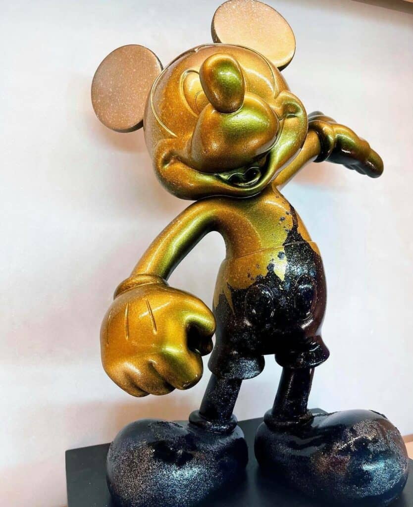 A gold and black metallic figure of Mouse of Muse stands on a sleek black base, striking a playful pose with one arm raised, capturing the enchanting whimsy fans love at Creations Shop.
