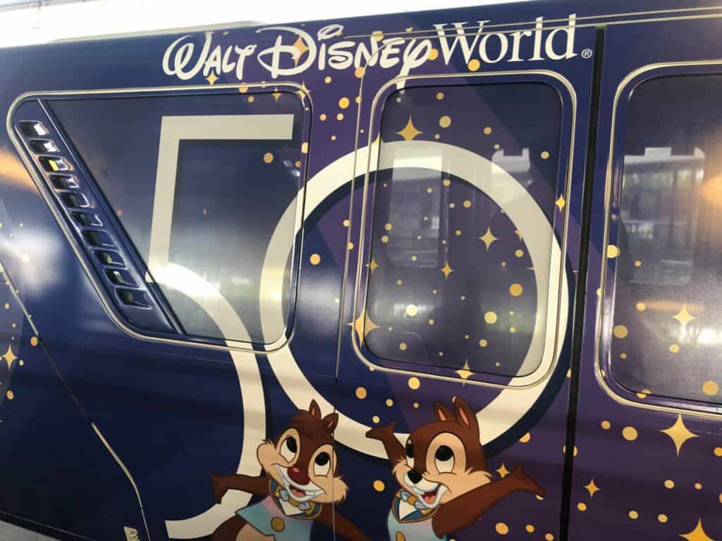Monorail gliding through Walt Disney World, decked out with a sparkling “50” logo and playful Chip and Dale artwork, celebrating the Magic Kingdom’s 50th Anniversary in classic Disney style.