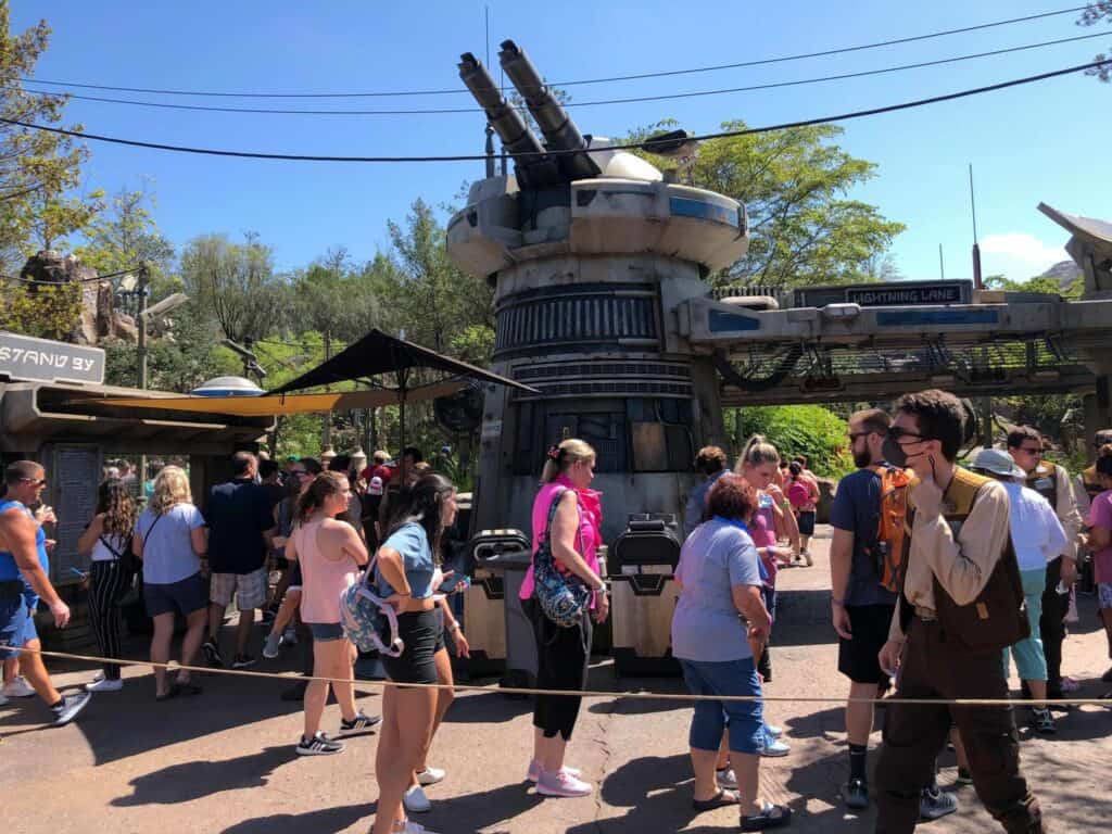 Guests flood the pathway outside Star Wars: Galaxy’s Edge at Disney’s Hollywood Studios, passing the iconic turrets of Batuu as excited fans line up for the popular Rise of the Resistance attraction under clear, sunny skies.