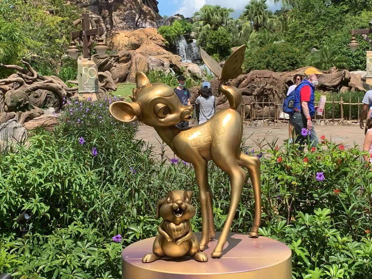 The gleaming golden statue of Bambi and Thumper, part of the Fab 50 Character Collection, stands out in the lush gardens at Disney’s Animal Kingdom, surrounded by guests and vibrant greenery. This magical sculpture is just one of many throughout the park honoring fan-favorite Disney characters in celebration of Walt Disney World’s milestone anniversary.
