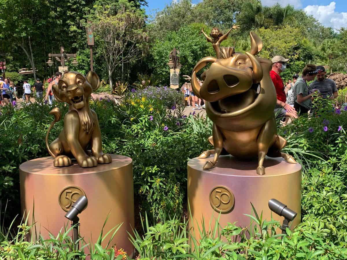 Simba, Timon, and Pumbaa from The Lion King are immortalized in shimmering bronze as part of the Disney Fab 50 Character Collection, proudly displayed on pedestals surrounded by lush gardens at Disney's Animal Kingdom.