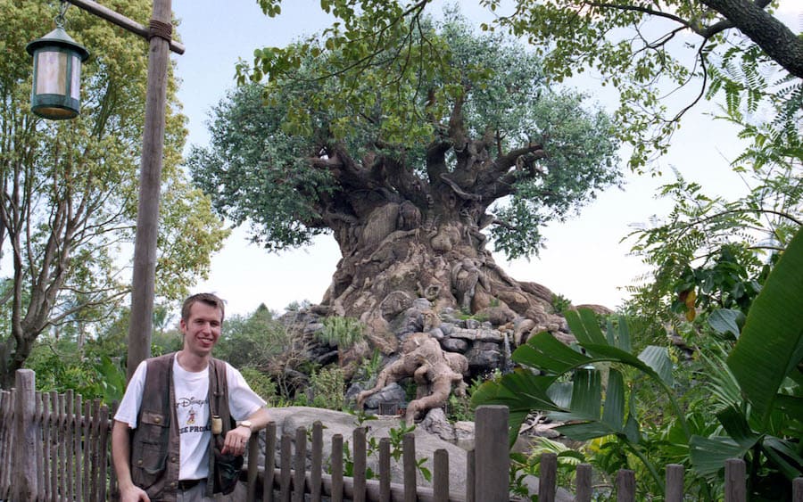 Guests pause by the rustic fence in front of Disney's Animal Kingdom’s iconic Tree of Life, admiring its intricate animal carvings and soaking in the lush, immersive atmosphere—a picture-perfect moment at Walt Disney World Resort.