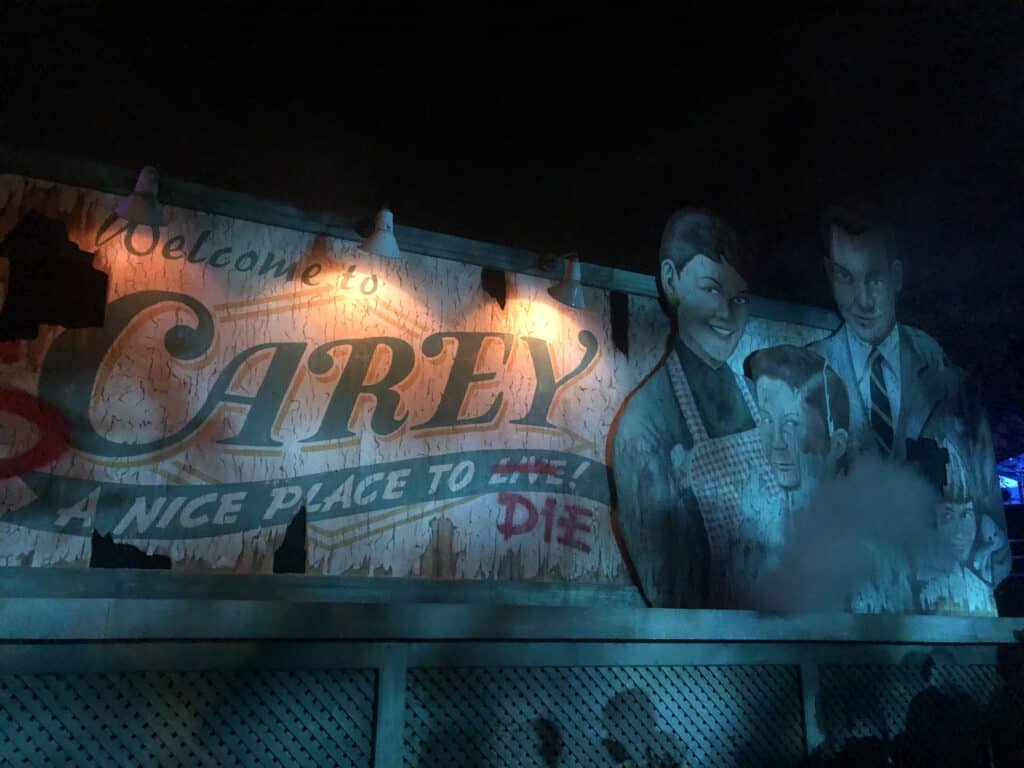 An aged “Welcome to Carey” sign glows under the park lights at Halloween Horror Nights, featuring faded, grinning characters and the chilling twist of “DIE” replacing “LIVE." This unsettling entrance sets a foreboding mood as Universal’s infamous event turns familiar welcoming sights into something sinister, blurring any sense of safety or normalcy for guests.