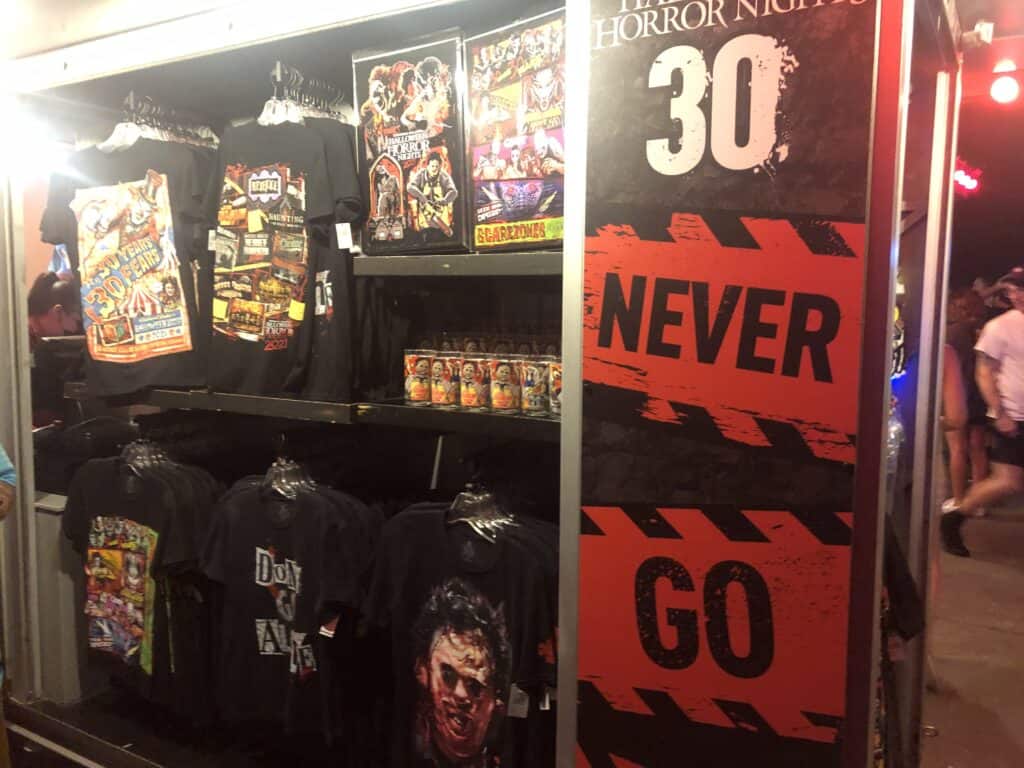 Halloween Horror Nights merch booth featuring exclusive shirts, collectible posters, and a bold "30 NEVER GO" sign, all showcasing the event's electrifying atmosphere and thrilling legacy while reminding fans to observe park safety guidelines.