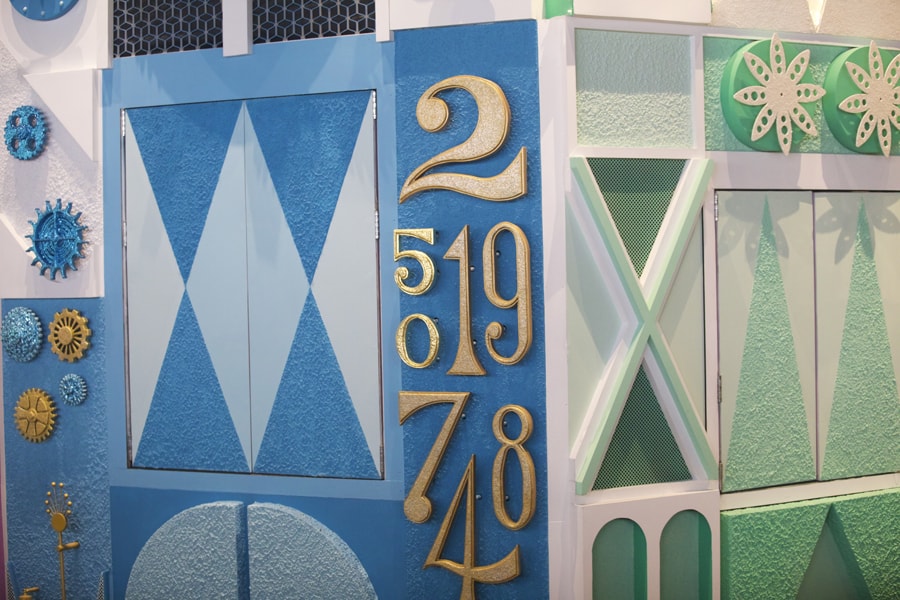 Decorative blue and white wall at the theme park, featuring eye-catching gold numbers—2, 5, 1, 9, 0, 7, 4, and 8—combined with whimsical geometric patterns that add to the immersive attraction experience.