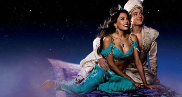 Aladdin and Jasmine, dressed in their elaborate costumes, soar above the crowd on a magical flying carpet surrounded by twinkling stars, capturing all the enchantment and spectacle of Disney’s Broadway-style stage show.