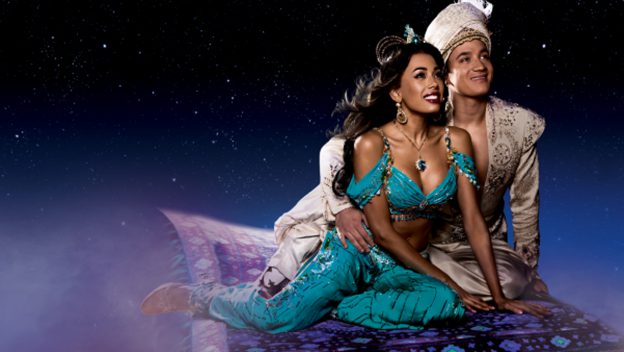 Aladdin and Jasmine, dressed in their elaborate costumes, soar above the crowd on a magical flying carpet surrounded by twinkling stars, capturing all the enchantment and spectacle of Disney’s Broadway-style stage show.