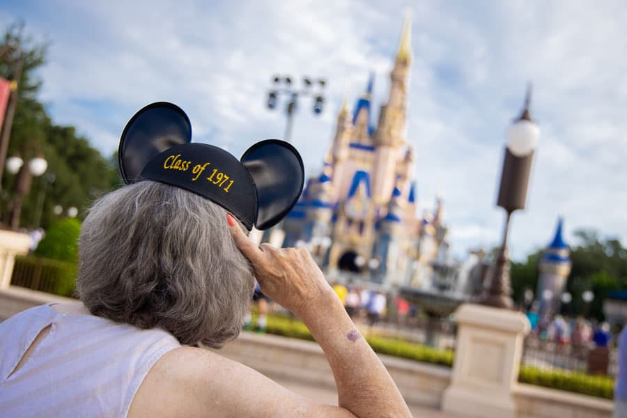 A Disney fan wearing "Class of 1971" Mickey ears celebrates 50 years of magic, gazing up at Cinderella Castle in Walt Disney World.