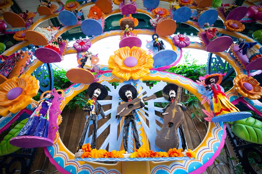 Vibrant Day of the Dead skeleton figures and festive flowers create a dazzling arch, honoring Día de los Muertos at Disneyland Resort for guests to enjoy.